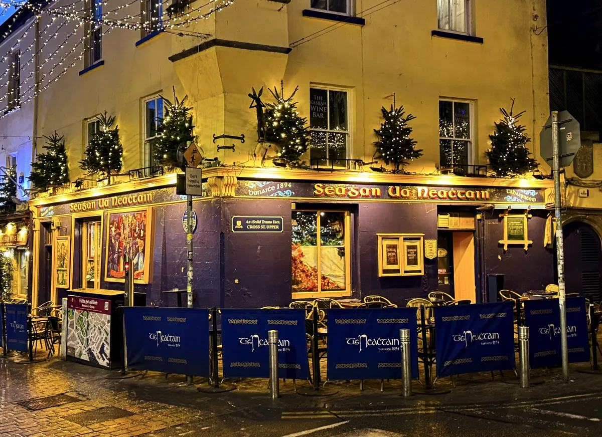 Žlutá nárožní hospoda na Quay Street v Galway, v noci osvětlená, s malými vánočními stromky na římse prvního patra