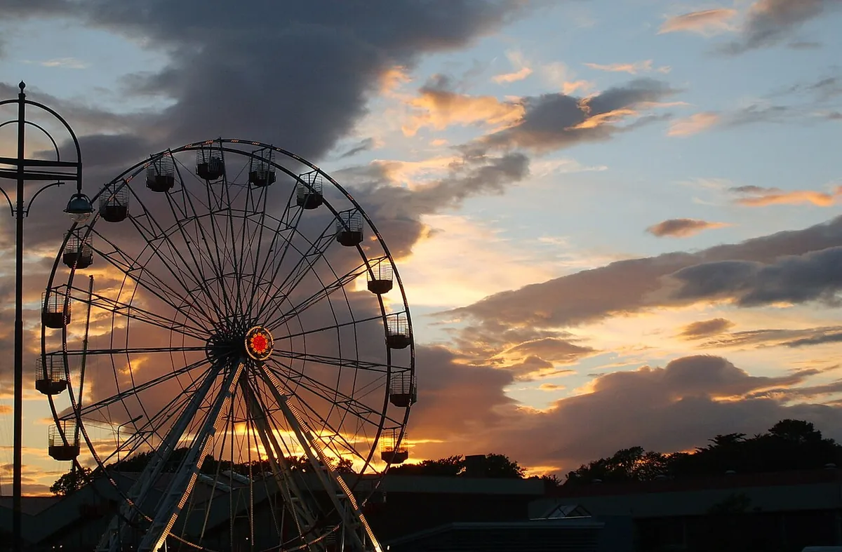 La gran noria de un parque de atracciones recortada contra un cielo al atardecer en tonos naranja y gris